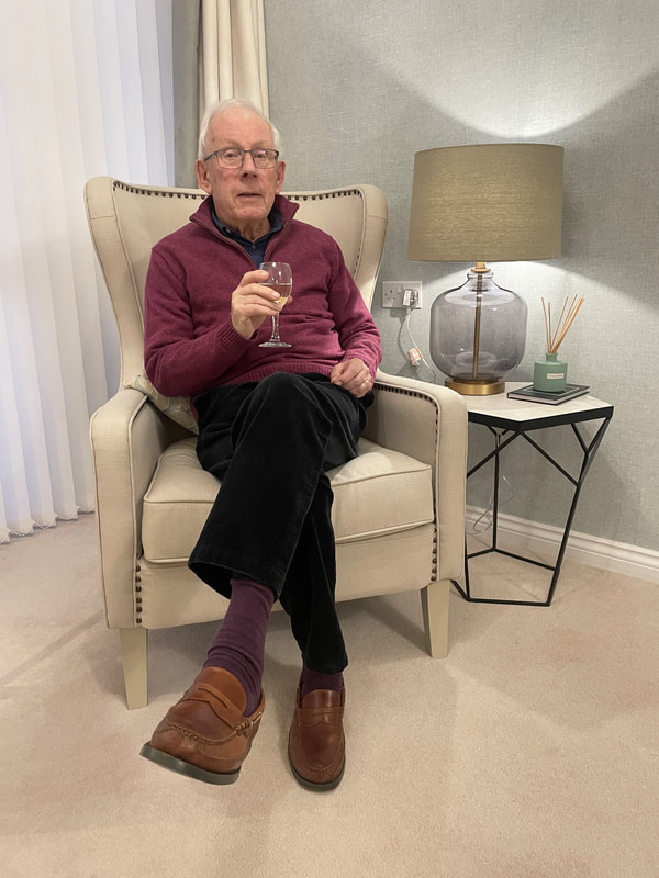 elderly man sitting in a cream armchair and drinking a glass of wine at a churchill retirement living apartment