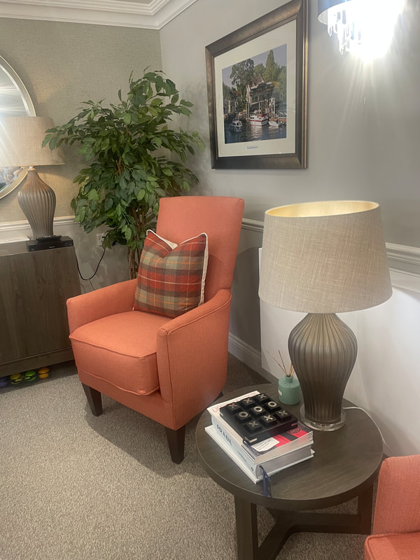 an orange armchair with plaid cushion next to a lamp table with noughts and crosses game
