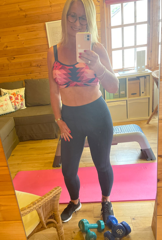 Daily workout wearing blue leggings pink sports bra and standing in log cabin with a pink workout mat