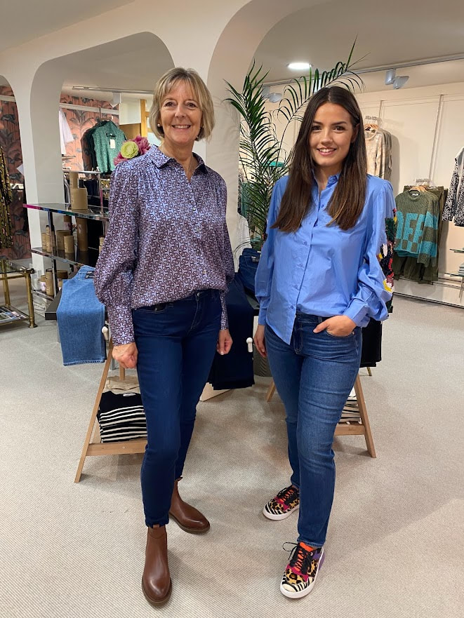 Two women in a fashion shop wearing jeans and blue blouses.