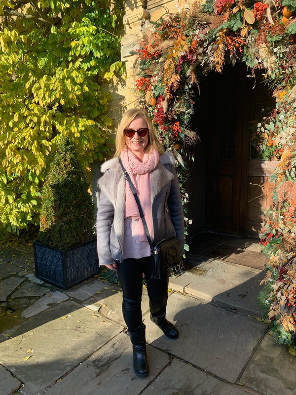 woman in grey jacket standing at the entrance to the lygon arms, cotswolds