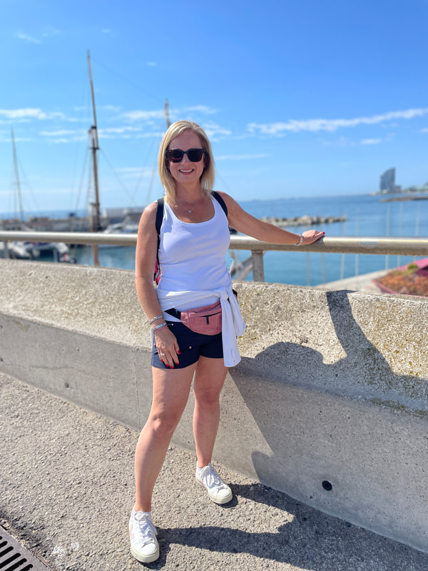 woman in shorts and white top standing by Barcelona beach with blue skies