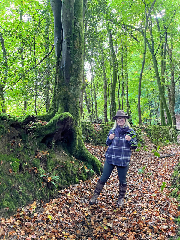 Michelle is walking in the ancient forests in the wye valley, the ground is carpeted with autumn leaves and she is wearing the checked boyfriend hoodie from ACAI