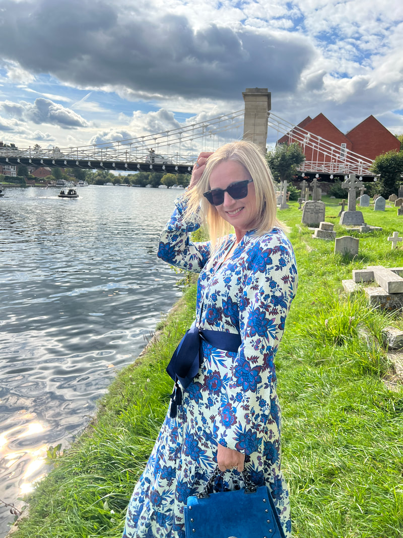 Michelle is standing next to all saints church by the river thames in marlow and is wearing a blue floral dress from Elizabeth Rose Fashion