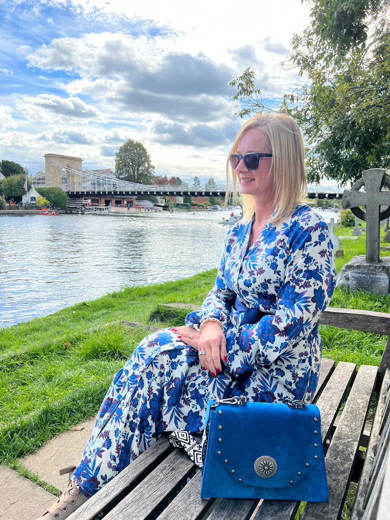 Michelle sitting on a bench outside all saints church marlow with marlow bridge in the background and wearing the jessica dress from aspiga