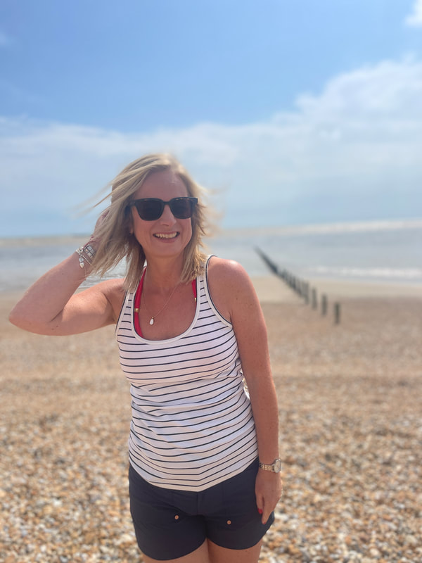 Michelle on the beach at Littlestone in Kent wearing navy blue shorts with a blue and white breton style vest top and red bikini