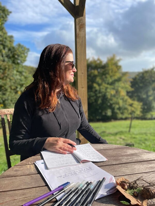 claire, the founder of the creatrix journey is sitting writing in her journal at hill farm in wales