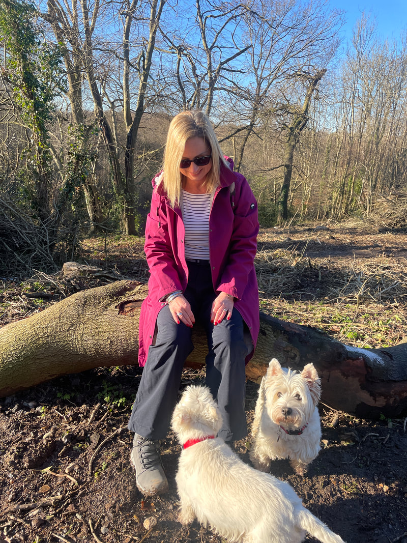 Michelle is sitting on a log in the woods with her two westie dogs
