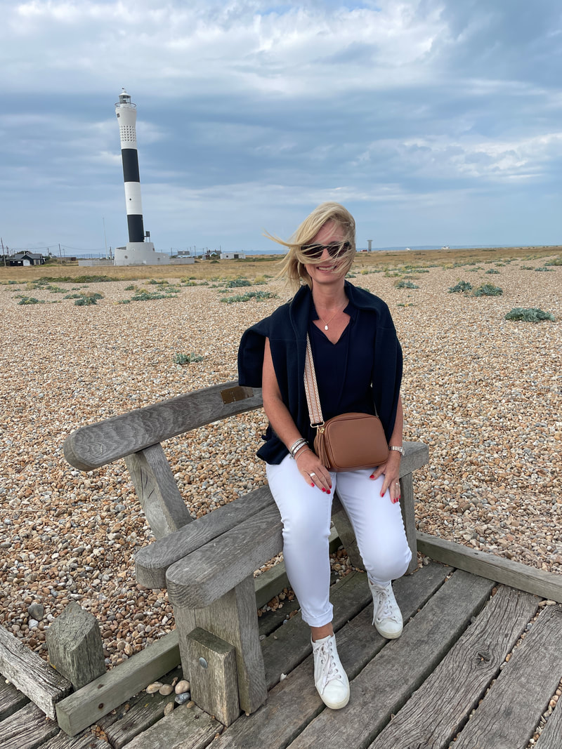 Michelle sitting on the bench at the end of the wooden walkway at Dungeness in Kent with the new lighthouse behind