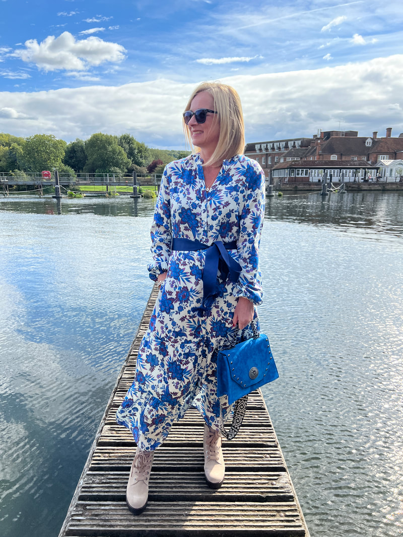 Michelle is standing in front of the river thames and the compleat angler hotel in marlow wearing a blue aspiga dress and enjoying the autumn sunshine
