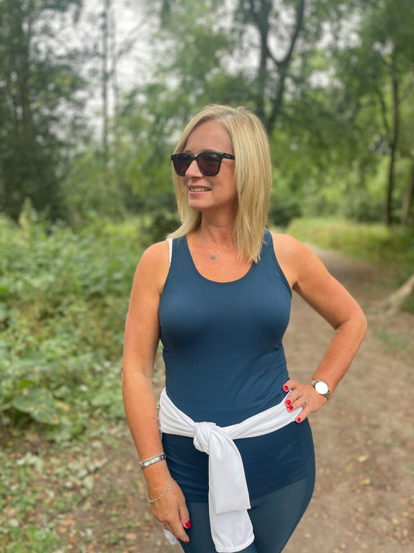 michelle is standing in the woods with her arm on her hip wearing a petrol blue workout top