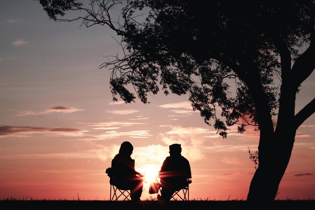 silhouette of two people sitting on chairs by a tree