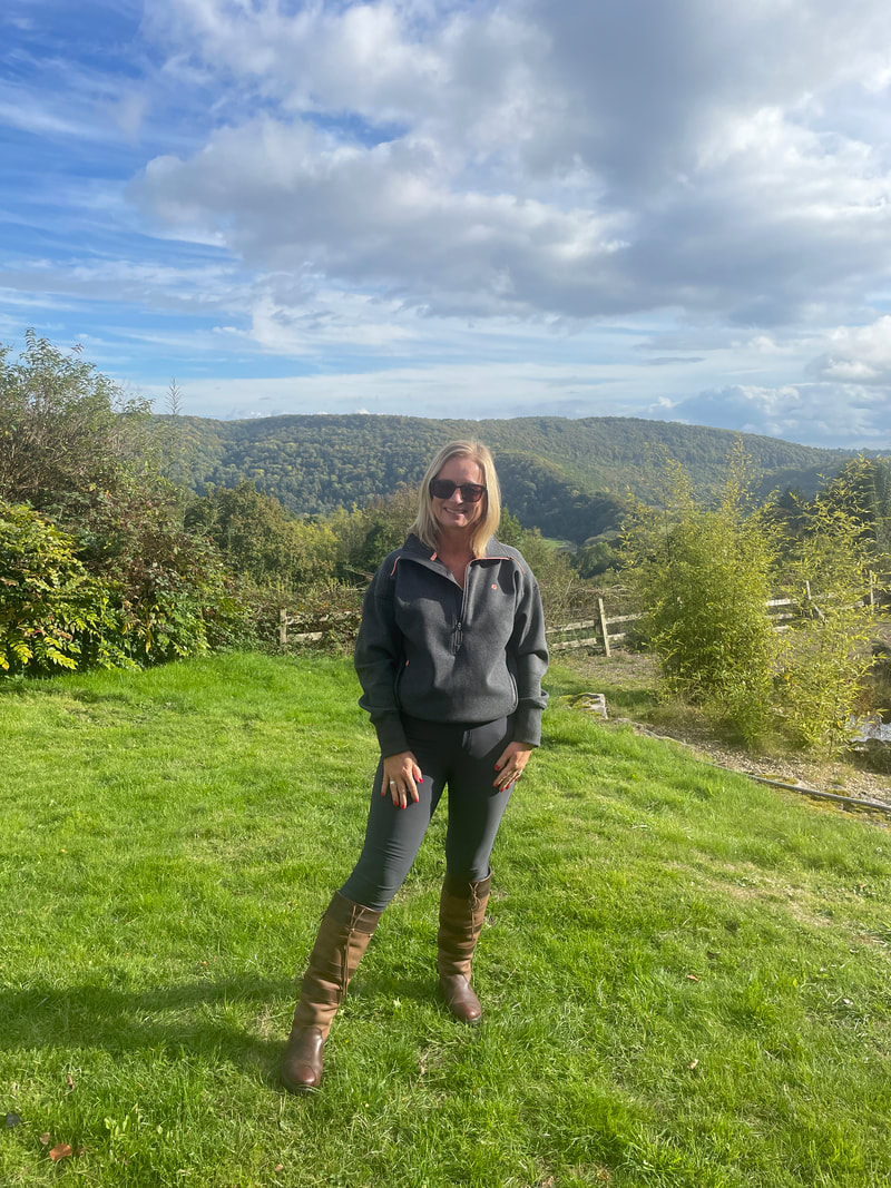 Michelle is standing a grass wearing acai outdoorwear outfit with a view of the tintern hills behind her
