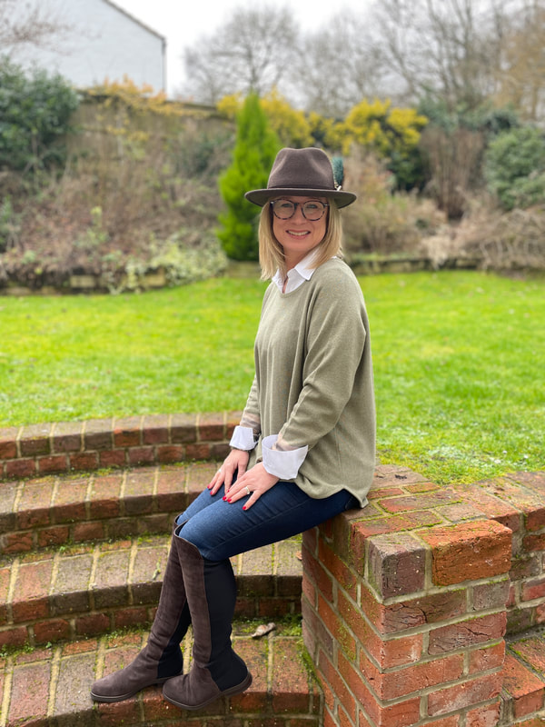 sitting on brick wall in the garden wearing a green cotton jumper and wool fedora hat