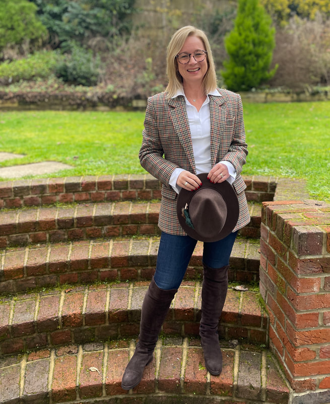 standing on the steps in the garden wearing a brown checked blazer with a wool fedora hat