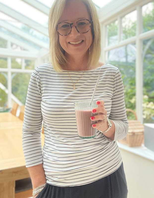 woman holding a pink smoothie in a glass wearing breton top | healthy smoothie recipes