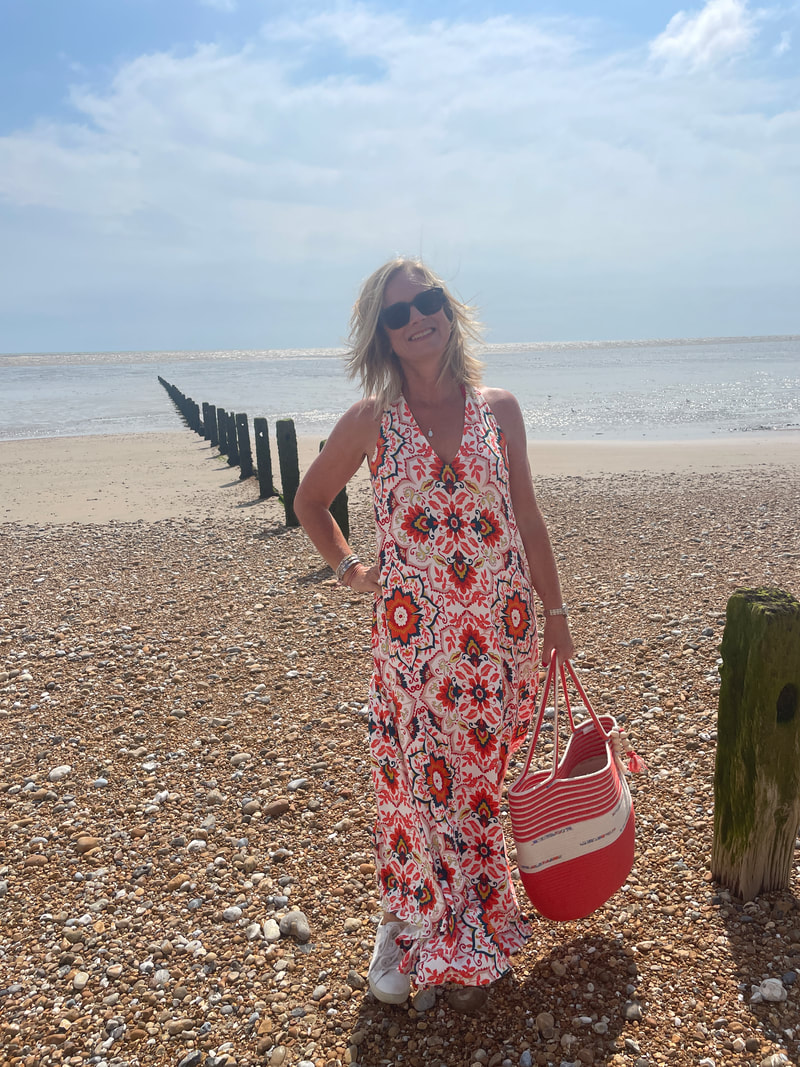 Michelle on the shingle beach at Littlestone in Kent wearing a red pattern jersey maxi dress from Boden and carrying a beach bag