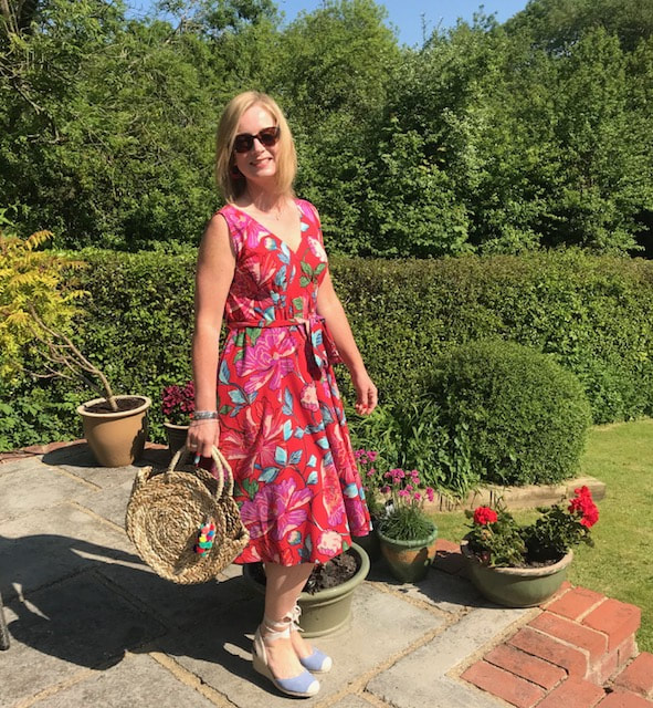 woman wearing red floral dress from & Other Stories in garden with straw bag