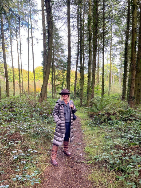 michell standing in the pine forest near tintern in wales wearing a mushroom coloured lightweight jacket and wearing a fedora hat