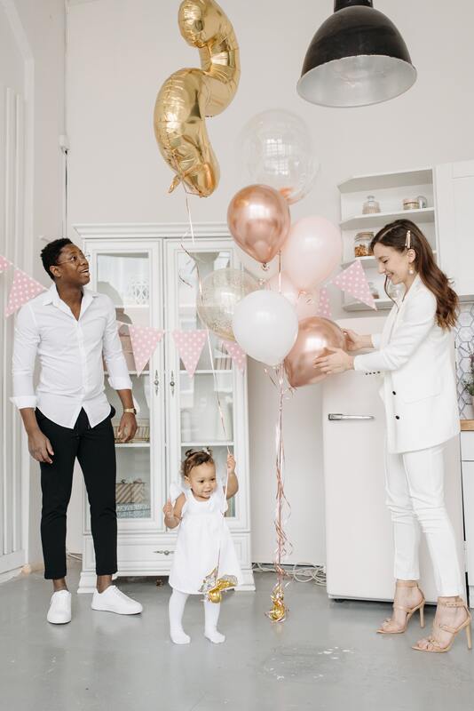 Dressing for a children's birthday party | mom and dad and daughter holding gold, white and silver balloons for a 5th birthday party