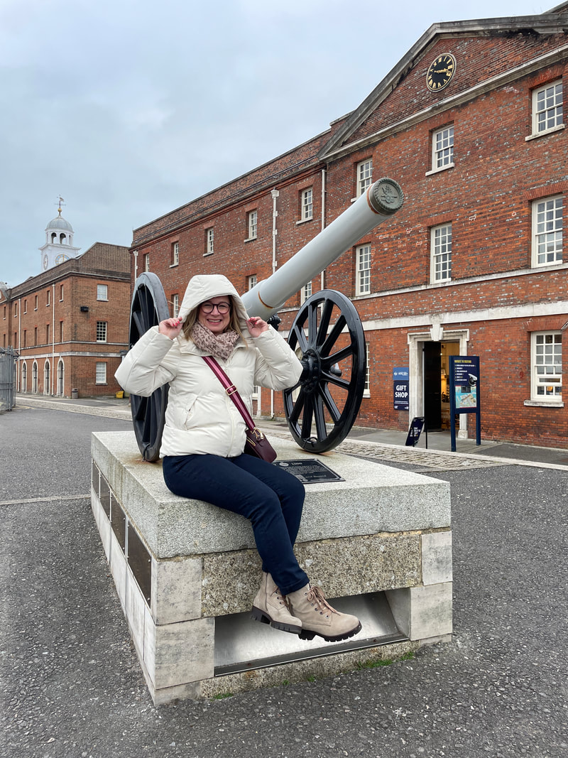 Michelle is sitting on a plinth with a gun carriage at Portsmouth Historic Dockyard