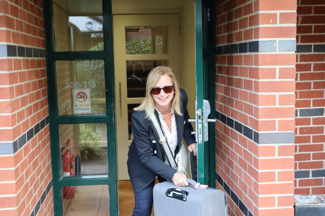 Michelle holding her grey suitcase and entering a red brick building | potters resorts five lakes