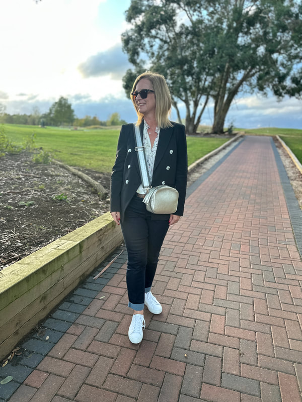 Michelle wearing jeans and a blazer and standing on a paved path by the golf course at Potters Resorts Five Lakes