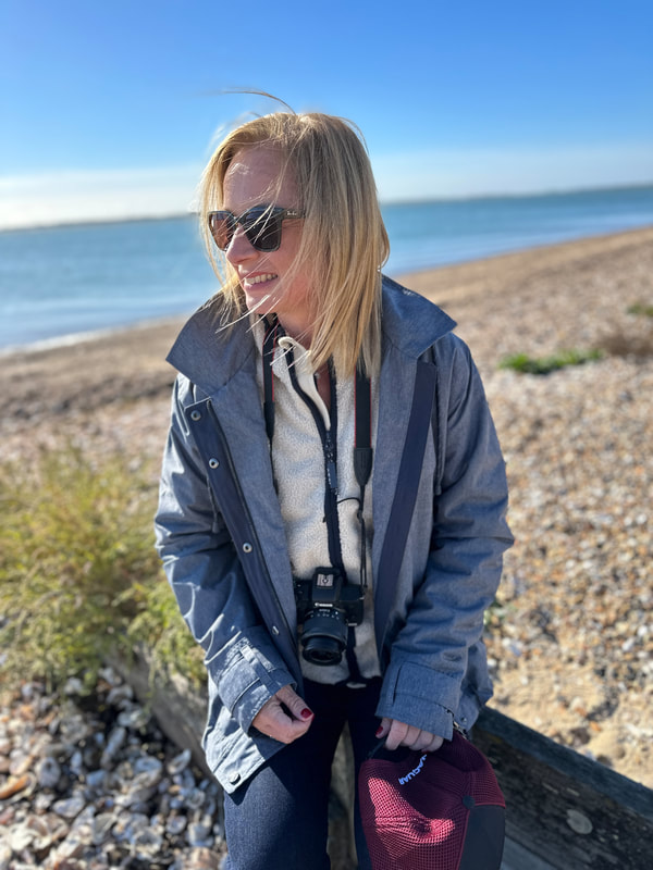 Michelle is sitting on the beach at West Mersea wearing a grey jacket from ACAI