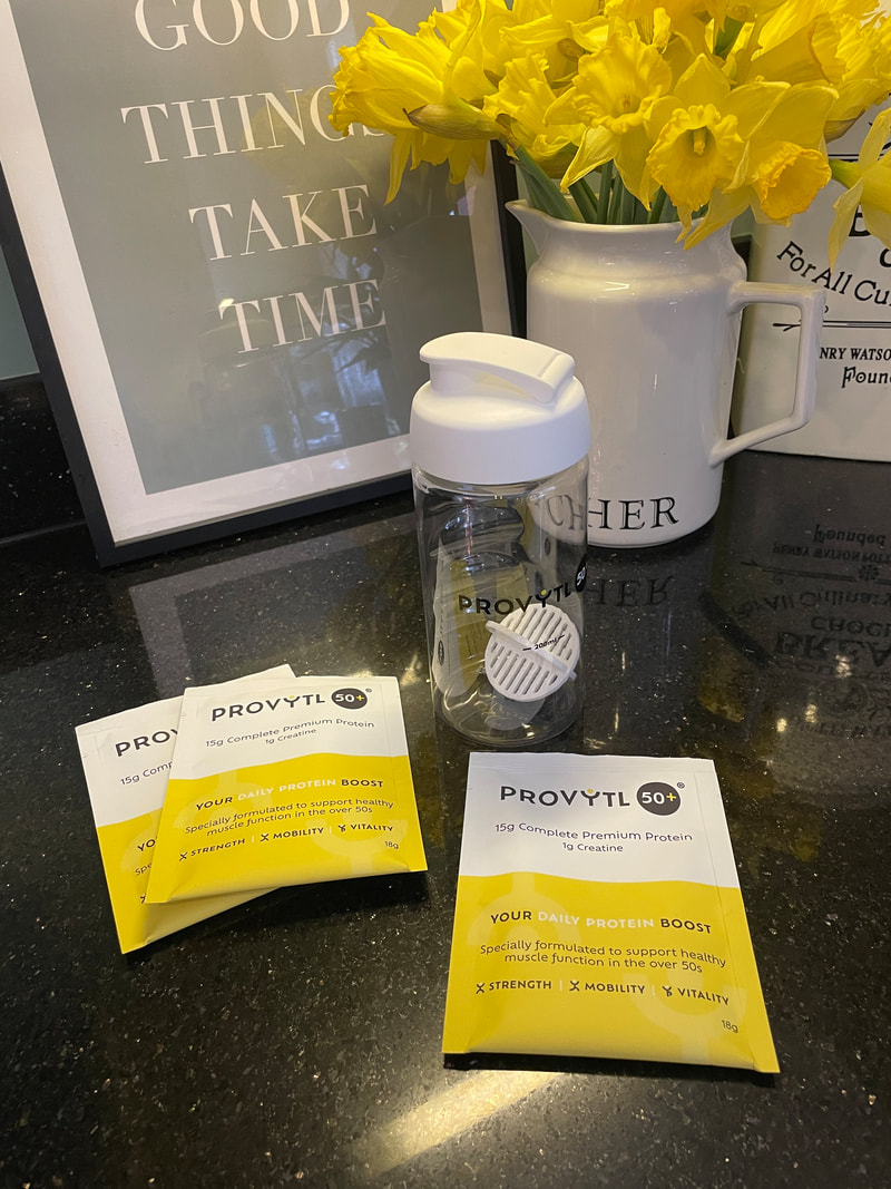 there are 3 sachets for provytl 50+ protein powder with a white and clear protein shaker in front of yellow daffodils in a white jug