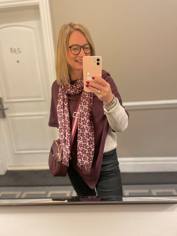 A mirror selfie taken in the corridor at The Waldorf, Michelle is wearing a burgundy poncho and holding a pink iphone