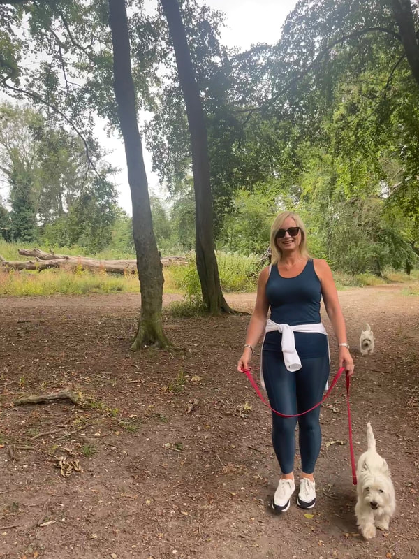michelle is walking in the woods with her two westies and wearing a petrol blue outfit from sweaty betty